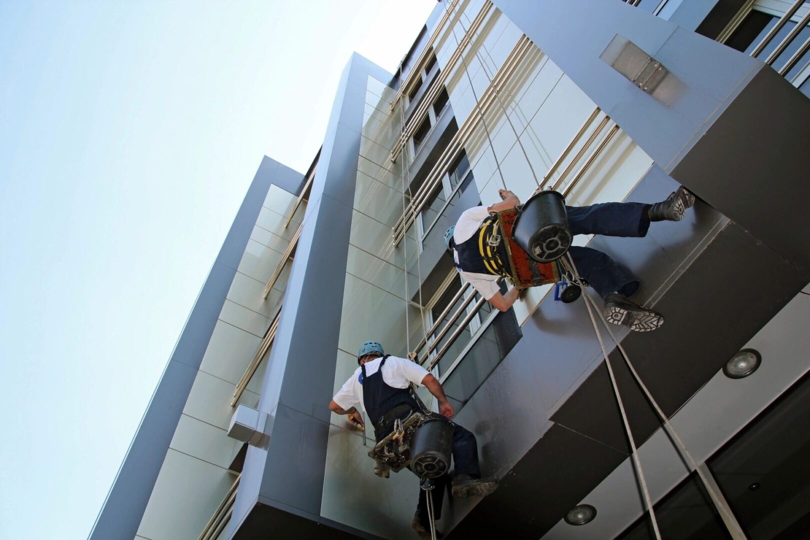 Two men hanging from a rope outside of a building.