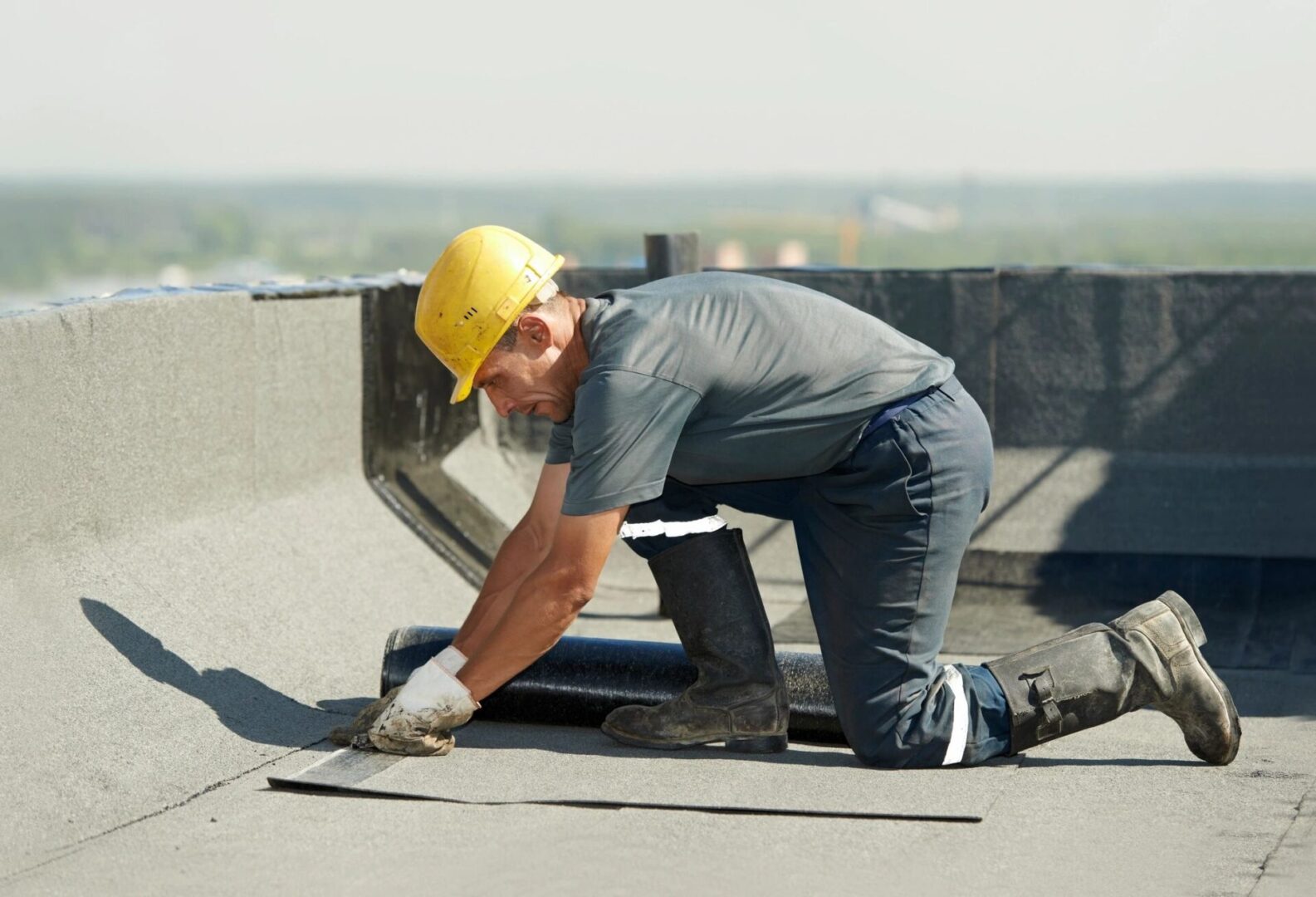 A man in grey shirt and yellow hard hat on top of roof.