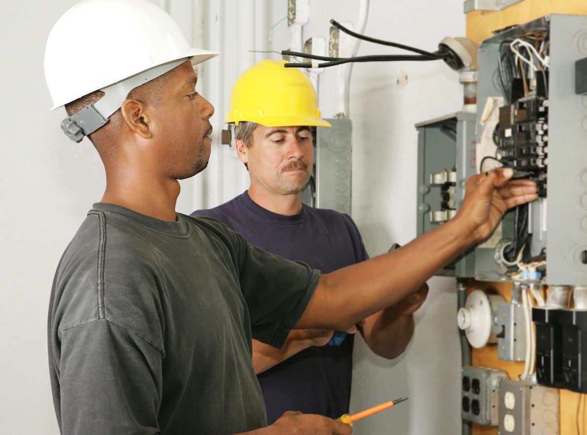 Two men in hard hats working on a circuit board.